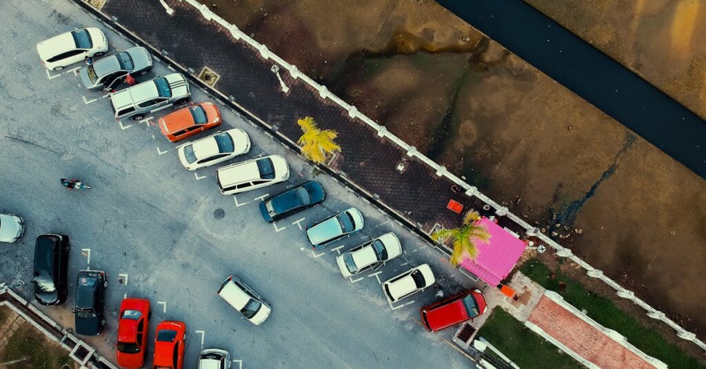 Aerial shot of a parking lot with cars and a pink building, next to a waterway.